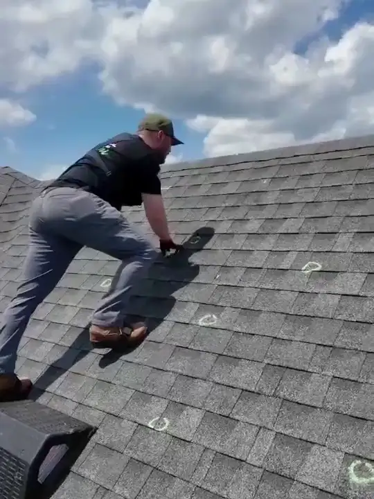A Hisway team member on a roof, circling hail hits in green chalk