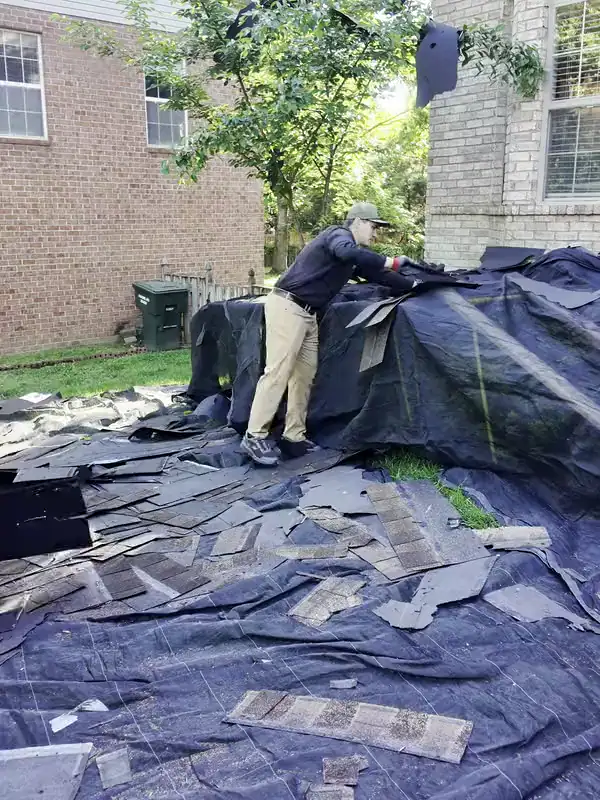 A Hisway project manager folding a tarp full of old shingles during a tear-off